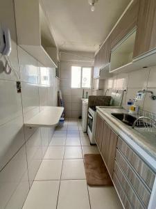 Elle comprend une petite cuisine blanche avec un évier et une fenêtre. dans l'établissement Apartamento Clube 3/4 com Ar-condicionado, à Aracaju