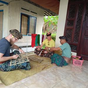three men sitting on the floor in front of a house at Pinge Traditional Village in Petang