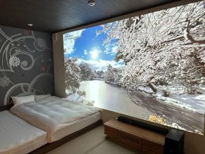 a bedroom with a large window with a snow covered tree at 泊まれるスマート映画館 tsuzumi in Housai