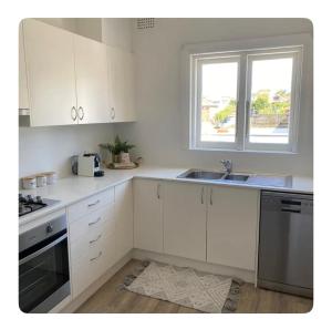 a kitchen with white cabinets and a sink and a window at Little Manly Getaway in Sydney