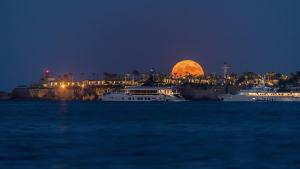 due barche in acqua di notte con la luna piena di Minareto a Siracusa