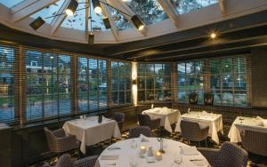 un restaurante con mesas y sillas blancas y ventanas en De Nederlanden, Restaurant & Boutique Hotel, en Vreeland