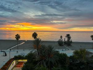 una puesta de sol sobre una playa con palmeras y el océano en Casa Granada, en Estepona