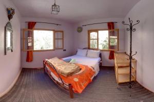 a bedroom with a bed with an orange comforter and two windows at Hotel De La Vallée in Aït Baha