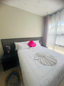 1 dormitorio con 1 cama blanca y 2 almohadas rosas en Sewelo inn guesthouse, en Maun
