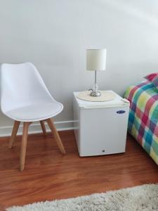 una silla blanca sentada junto a una cama con lámpara en Depto 2dorm/2baños, estac Viña, en Viña del Mar