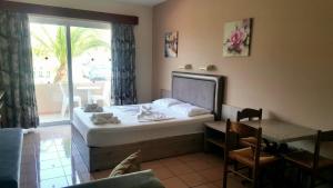 a bedroom with a bed and a table and a window at Jo An Beach Hotel in Adelianos Kampos