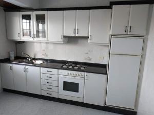 una cucina con armadietti bianchi, piano cottura e frigorifero di Piso luminoso con enorme terraza y buenas vistas a Carballo