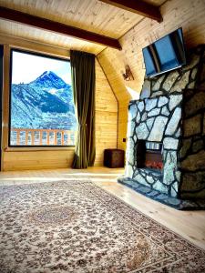 a room with a stone fireplace with a mountain view at Hillside Kazbegi in Stepantsminda