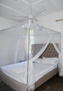 een slaapkamer met een hemelbed en een plafondventilator bij Garden house 2 in Ukunda