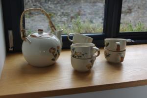 three tea cups and a teapot on a window sill at Cosy ferme de village en baie du Mont Saint Michel in Vains