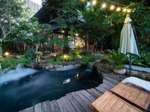 a pond in a garden with an umbrella and chairs at Crystal Resort Korat in Nakhon Ratchasima