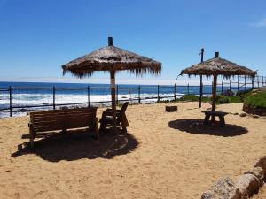 two benches and umbrellas on a beach with the ocean at Departamento AltoMar El Tabo Isla Negra in El Tabo