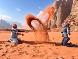 two people sitting in the sand in the desert at Wadi rum Ahmed Badawi in Wadi Rum