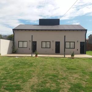 ein weißes Gebäude mit schwarzen Türen und einem Grasfeld in der Unterkunft Amancay in Villa Elisa