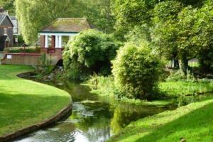 a garden with a river with a house in the background at Woodman's Cottage in Temple Ewell
