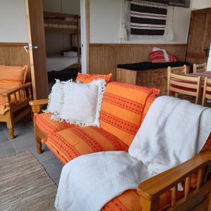 a living room with an orange couch with pillows at CABAÑA ESTANCIA LAZO in Torres del Paine