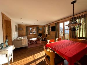 a dining room with a red table and a living room at Chalet Solaria 2 bedrooms with mountain and garden view in Zweisimmen