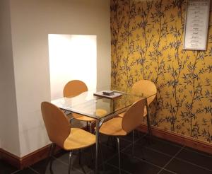 une table et des chaises en verre dans une pièce ornée de papier peint jaune dans l'établissement Bwthyn Bach (Tiny Cottage), à Wrexham