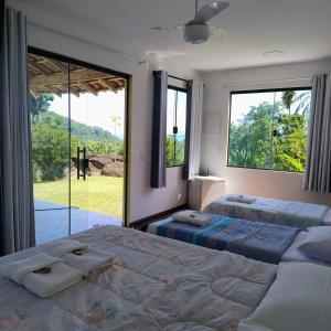 two beds in a bedroom with large windows at Pousada Porto Taquari in Paraty