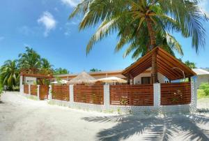 a house with a wooden fence and a palm tree at Oceano Beach Vashafaru in Vashafaru