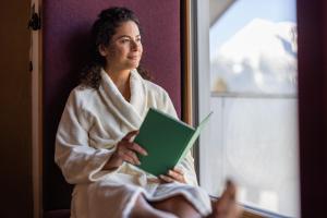 a woman sitting in a robe reading a book at Biohotel Leutascherhof in Leutasch