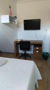 a bedroom with a bed and a desk with a flat screen tv at Casa de amigos e parentes in Eunápolis