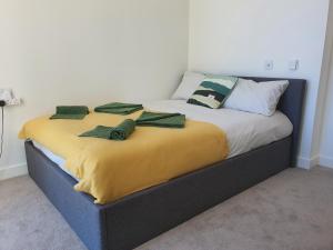 a bed with a yellow blanket and green pillows on it at Cozy Room with Private Bathroom in Luxurious Flat in London