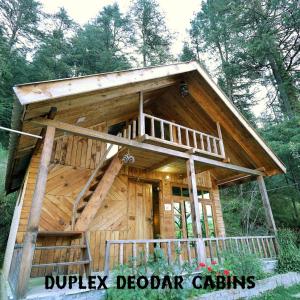 a large wooden cabin in the woods with a porch at Himalayan Cedar Nest in Sainj