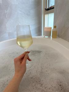 una persona che tiene un bicchiere di vino di fronte a una vasca da bagno di Koopalanda Dreaming a Vivonne Bay