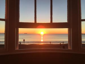 una ventana con vistas a la playa al atardecer en Whitecliff Guest House, en Weymouth