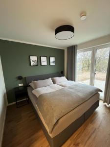 1 dormitorio con 1 cama grande y pared verde en diemelblick acht - Ferienhaus für 6 Personen mit Sauna, Garten und Dachterrasse mit Panoramablick, en Heringhausen