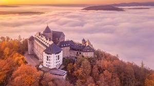 um castelo no topo de uma montanha acima de uma camada de nuvens em Hotel Schloss Waldeck em Waldeck