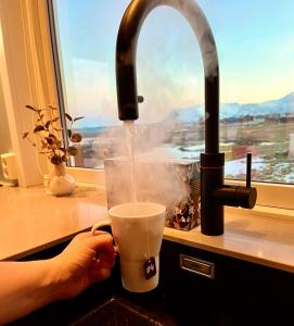 a person is drinking a drink from a faucet at House by the ocean with midnight sun view in Eggum
