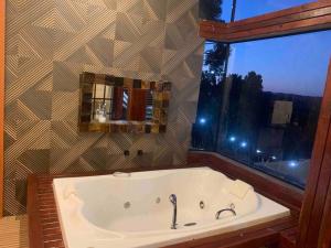 een bad in een badkamer met een groot raam bij Chalé Romântico C. grande do Sul in Campina Grande do Sul