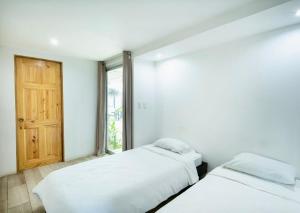 two beds in a white room with a window at Hotel Bamboo in Jacó