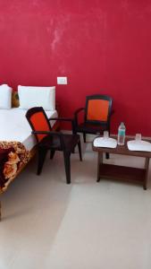 Habitación con 2 camas, sillas y pared roja. en Squirrel Nest Guest House en Mahabalipuram