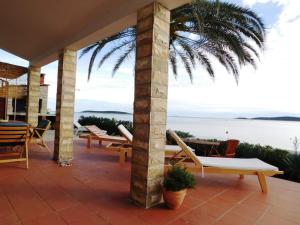 a patio with chairs and a palm tree and the ocean at Holiday House Rivi in Milna