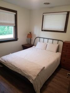 a bedroom with a white bed with a nightstand and two windows at Whitney Bay House on CHQ Lake in Mayville