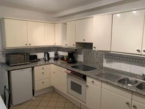 eine Küche mit weißen Schränken, einer Spüle und einer Mikrowelle in der Unterkunft Maison de 6 à 8 personnes in Faches-Thumesnil