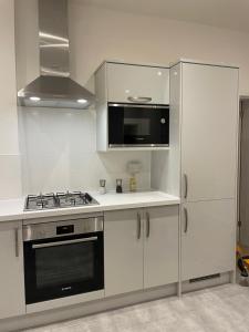 Newly renovated flat in Ashtead في Ashtead: مطبخ أبيض مع موقد وميكروويف