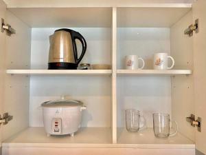 a coffee maker and cups on shelves in a kitchen at Azure Condo in Manila