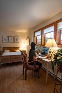 une femme assise sur un bureau avec un ordinateur portable dans une chambre dans l'établissement Auberge Yoga Salamandre, à Lac-Brome