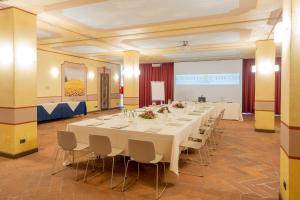 una grande stanza con un lungo tavolo con tavoli e sedie bianchi di Relais & Spa Castello di Casiglio a Erba