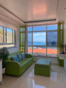 a living room with a green couch and a large window at Apartamentos vista ao mar in Praia Baixo