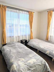 a bedroom with two beds and a large window at 癒やしの宿 cheer house 源泉掛け流し温泉 hokkaido noboribetsu shiraoi in Shikyū