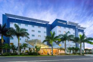 a hotel with palm trees in front of it at Courtyard by Marriott San Jose Airport Alajuela in Alajuela City
