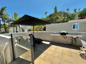 um pátio com um guarda-chuva, uma mesa e uma cadeira em Oasis Rooftop Spa Apartment em Noosa Heads