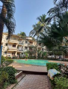 a swimming pool in front of a building with palm trees at Calangute apartment in Calangute