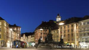 eine Stadt in der Nacht mit einem Uhrturm im Hintergrund in der Unterkunft City De Lights in Graz